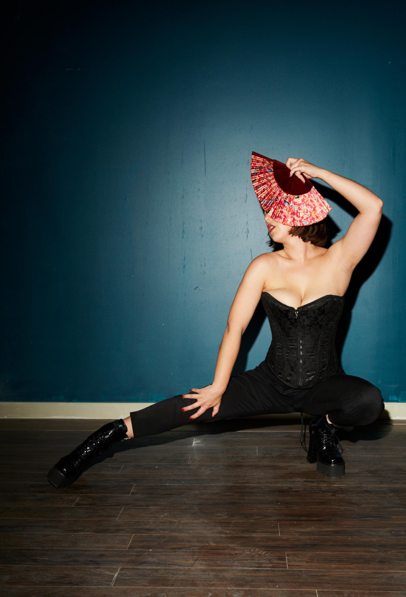 Boston Dominatrix Mistress Maia Oni posing with a fan in front of a blue background